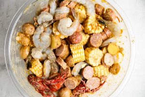 The shrimp, crawfish, corn, potatoes, butter, and seasoning are tossed together in a bowl to evenly coat everything.