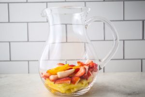 Sliced fruit is added to a large glass pitcher.