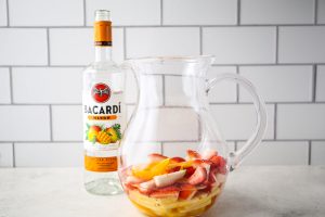 Rum is poured into the sangria pitcher on top of sliced fruit.
