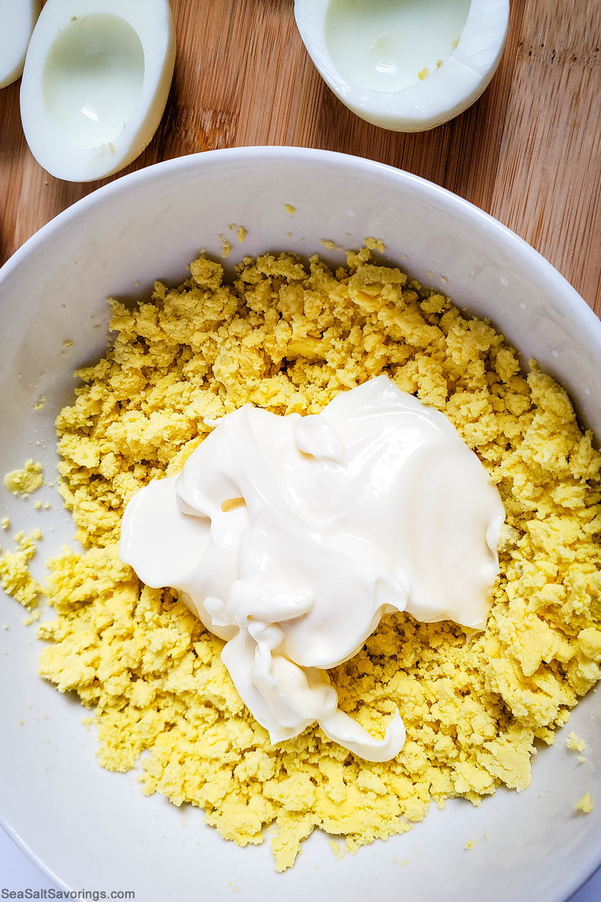 adding may to mashed up egg yolk in a bowl