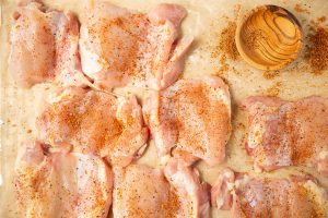 Chicken thighs are layed on parchment paper and sprinkled with seasoning.