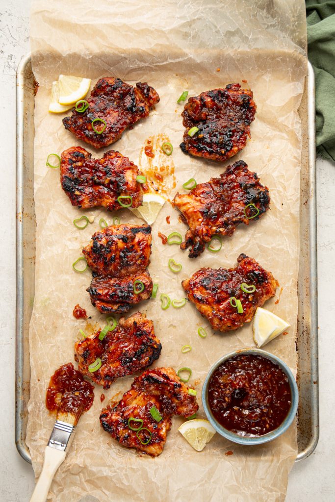 Chicken thighs are plated on a parchment paper lined baking sheet and brushed with more BBQ sauce.