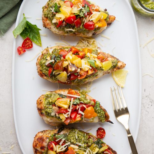 Chicken breasts are topped with pesto and a tomato basil mixture and plated on a white plate.