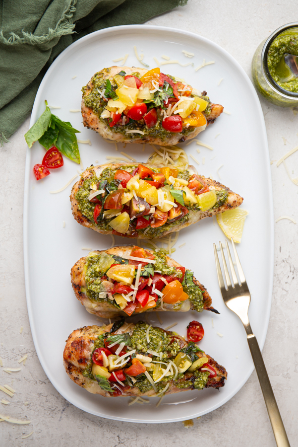 Chicken breasts are topped with pesto and a tomato basil mixture and plated on a white plate.