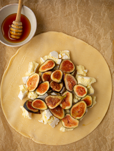 A pie crust is rolled out, then topped with brie and sliced figs.