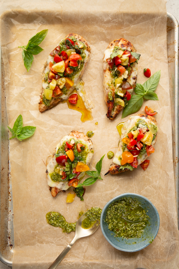 Chicken breasts are topped with mozzarella cheese, pesto, and tomatoes.