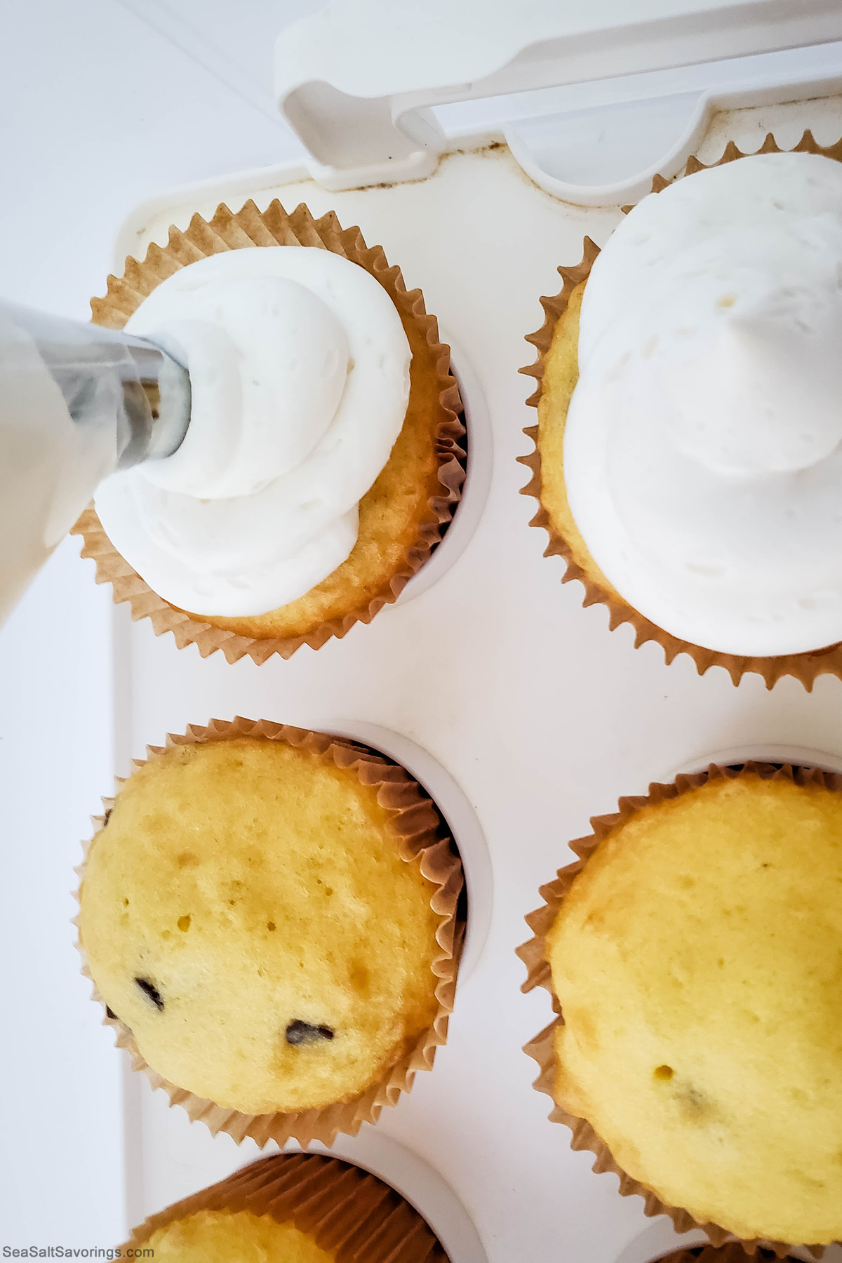 squirting frosting on top of cupcakes from a pastry bag