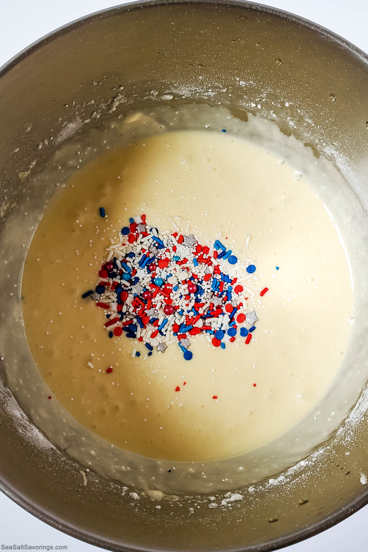 cupcake batter in a mixing bowl with sprinkles placed on top ready to mix