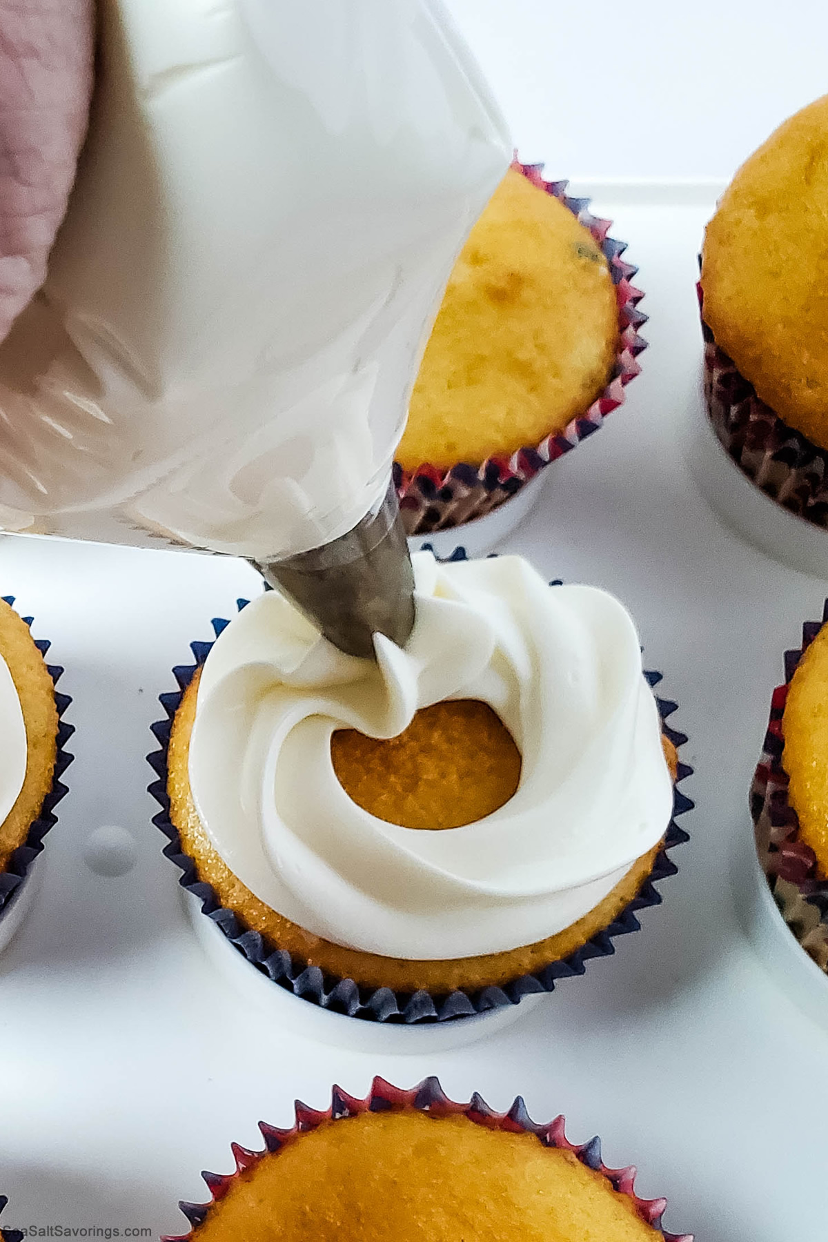 adding frosting on top of baked cupcakes