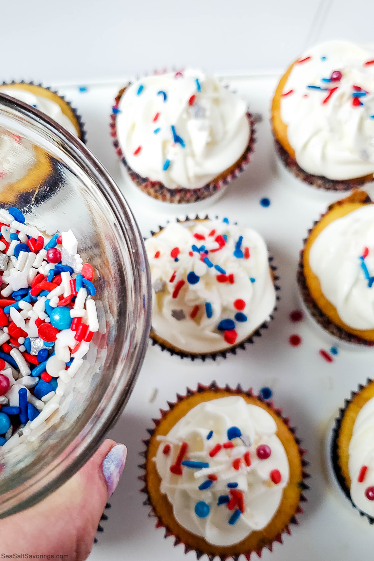 adding sprinkles on top of frosted cupcakes