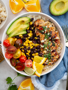 Rice, black beans, corn, tomatoes, avocado, and mojo chicken is added to a bowl to make a mojo chicken and rice bowl.
