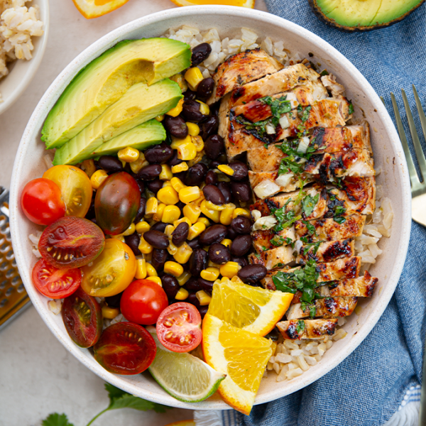 Rice, black beans, corn, tomatoes, avocado, and mojo chicken is added to a bowl to make a mojo chicken and rice bowl.