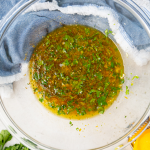Mojo marinade is combined in a large glass bowl and contains fresh citrus juicy, cilantro, seasoning, and olive oil.