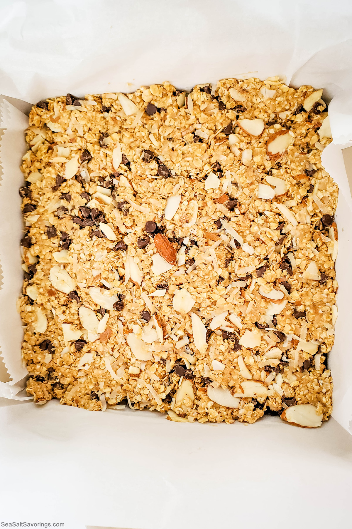 pressing granola bar mixture flat on a paper lined baking sheet