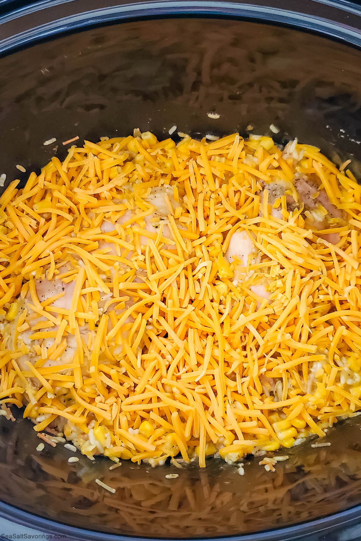 inside crock pot showing chicken covered in sauce and corn and cheese