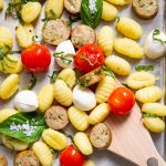 A spoon is scooping the gnocchi sheet pan mixture, which is topped with fresh basil.