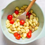 The gnocchi, tomatoes, sausage, and olive oil are combined in a bowl and stirred.