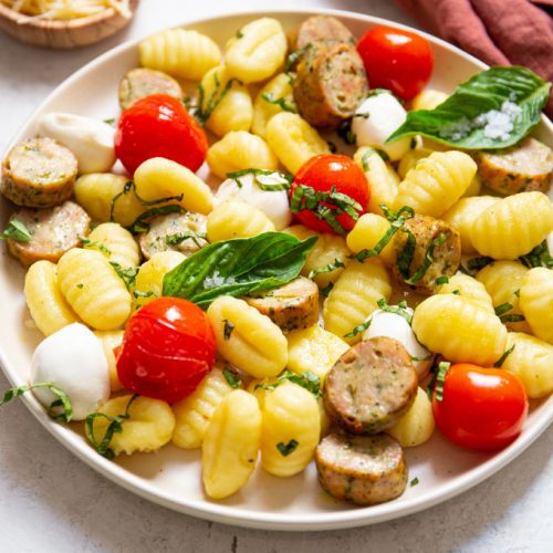 Blistered tomatoes, gnocchi, sausage, mozzarella, and basil are plated on a small plate.