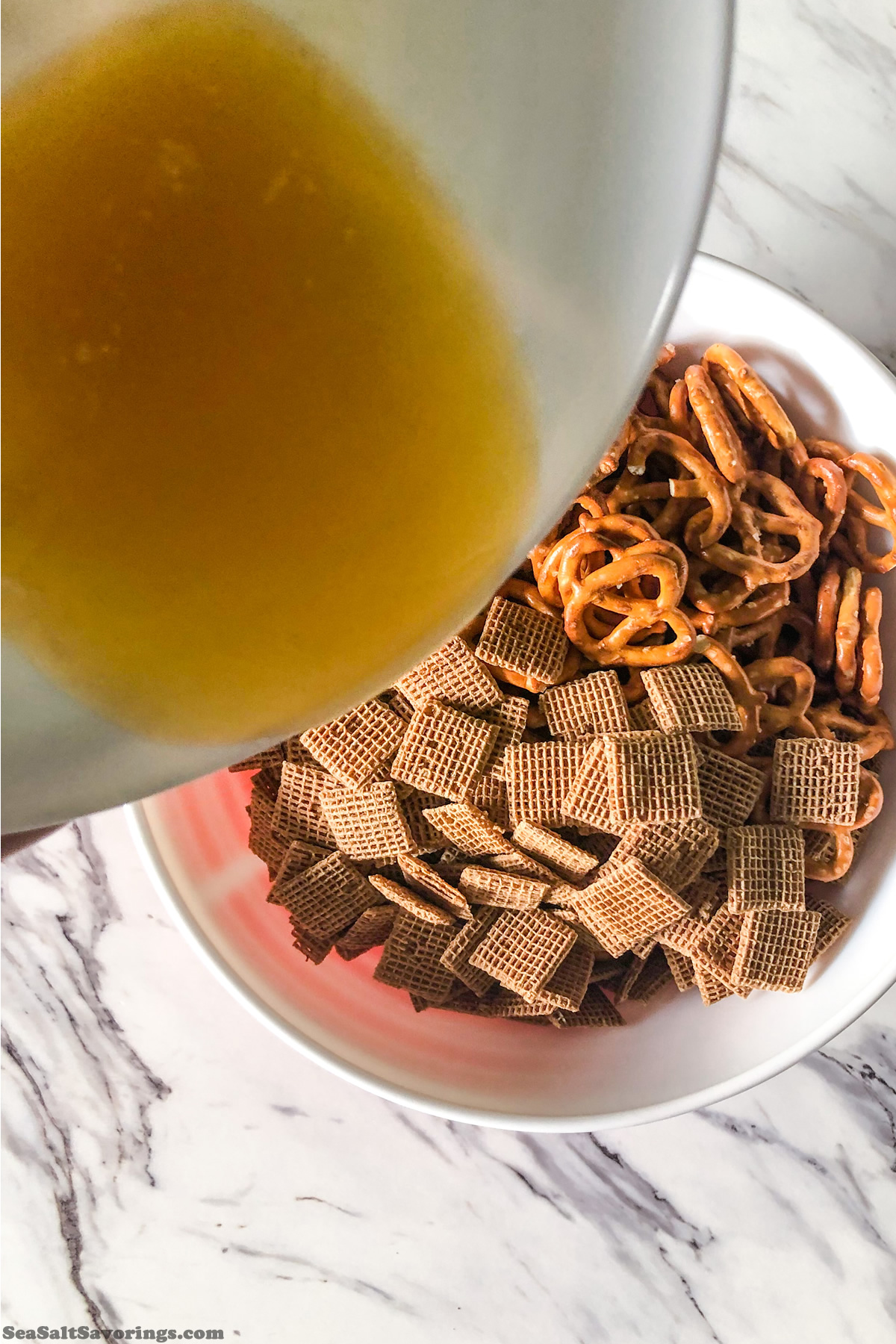 pouring melted butter into mixing bowl full of shreddies and pretzels