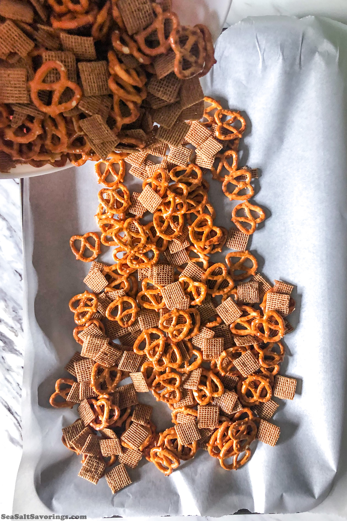 pouring shreddies and pretzels mixture into baking sheet