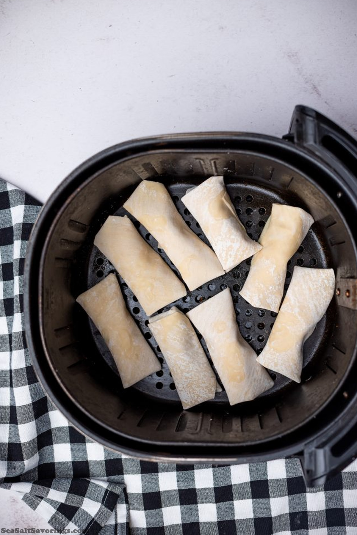 placing uncooked eggrolls in air fryer basket