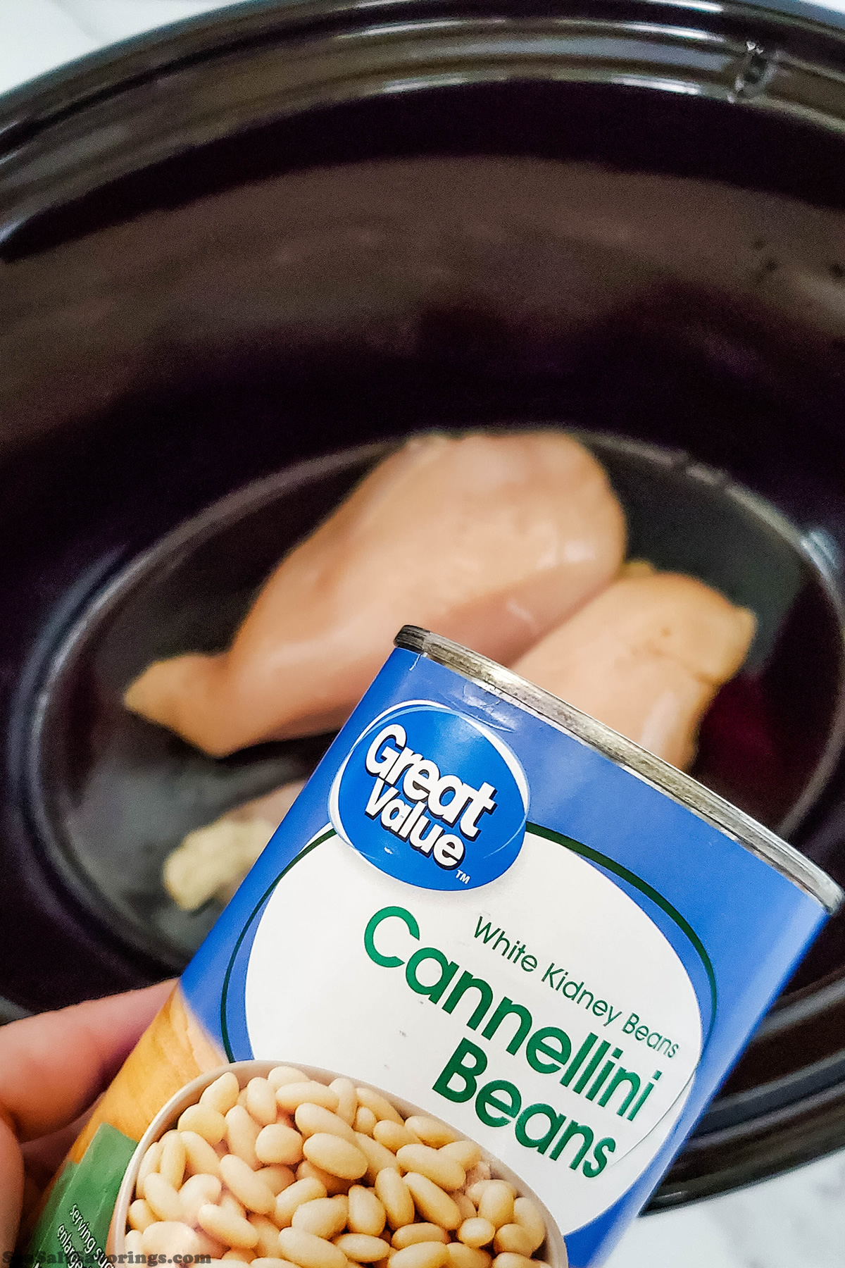 pouring can of beans on top of chicken breasts in crock pot