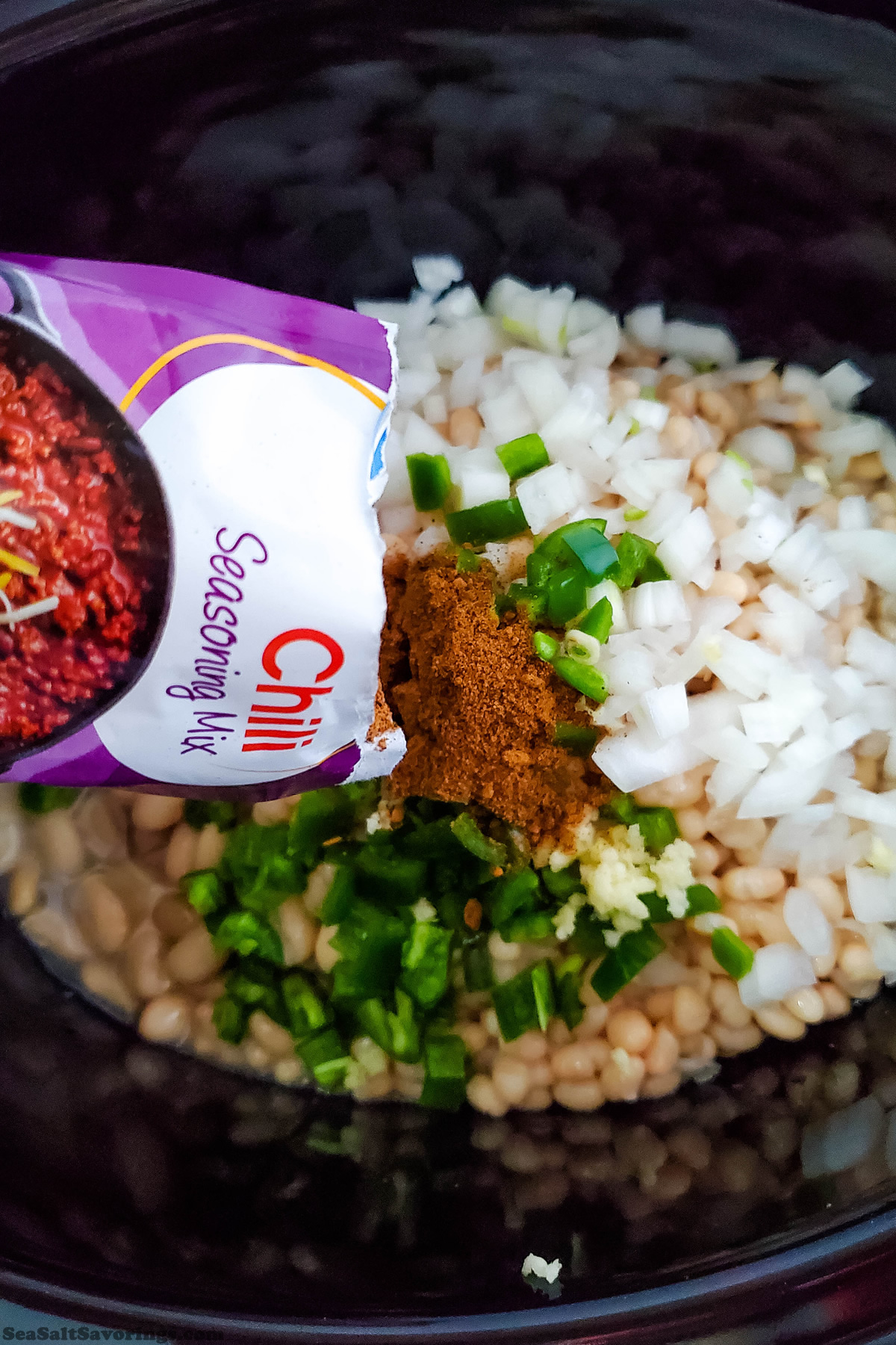 pouring seasoning packet on top of beans and vegetables in crock pot