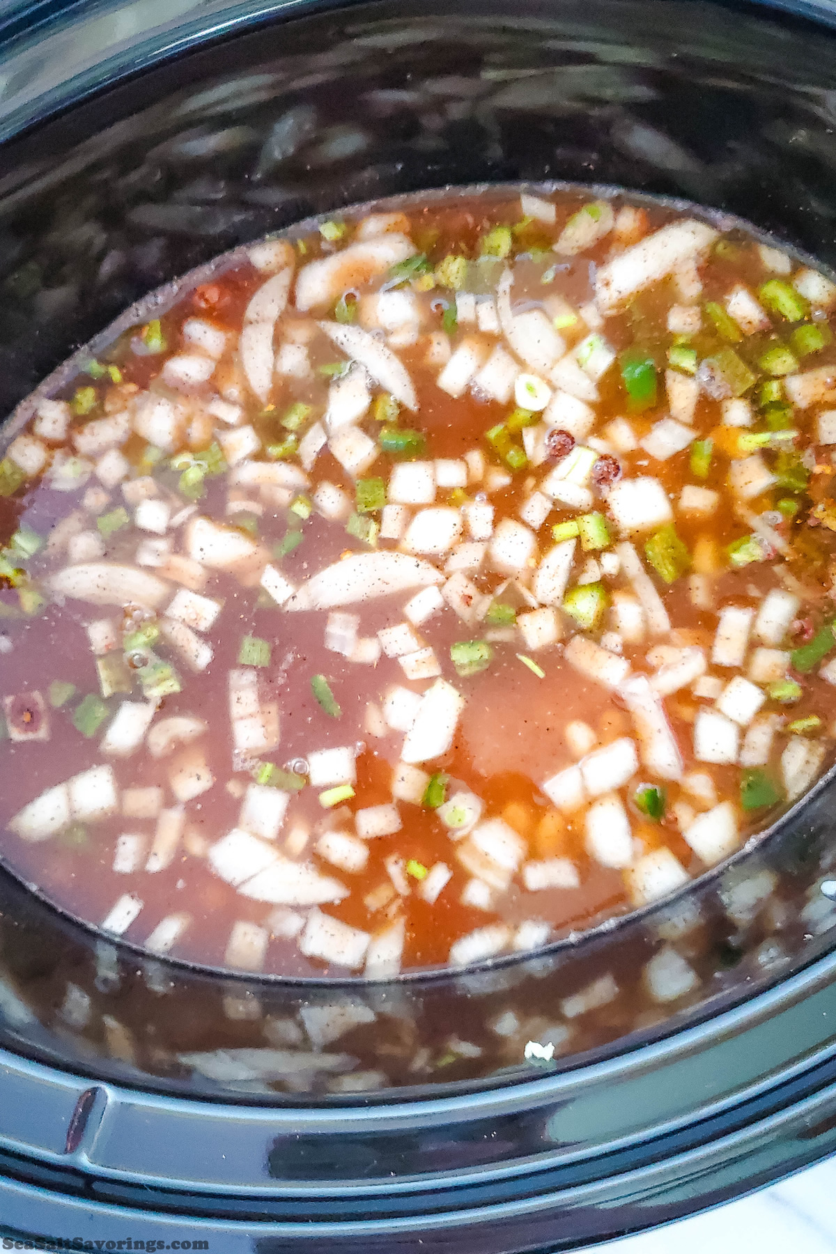 view inside crock pot full of seasoned water with floating vegetables on top