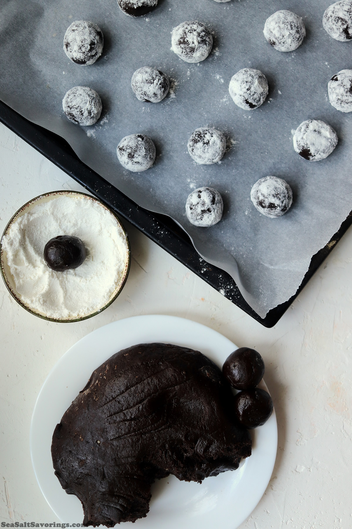 bowl of cookie dough with rolled balls of the dough showing how to roll it in the dry frosting and place on cookie sheet