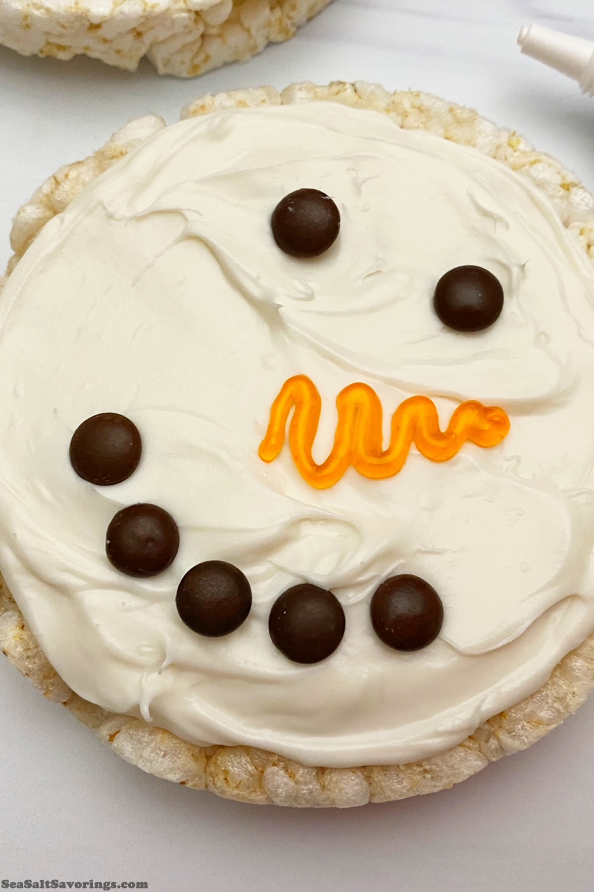 rice cake with frosting and chocolate chips designed to make a snowman face