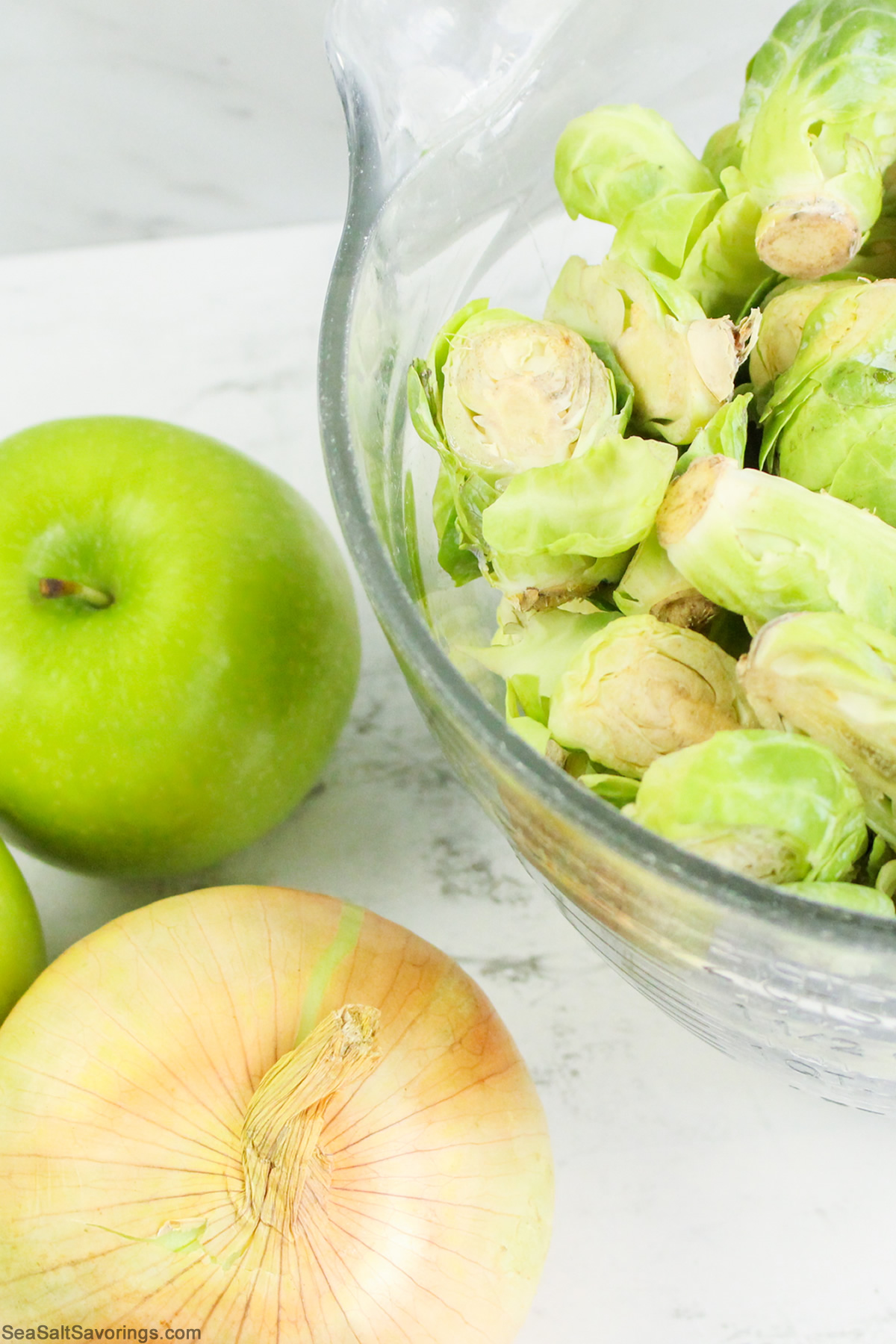 apple and onion next to a bowl of brussel sprouts