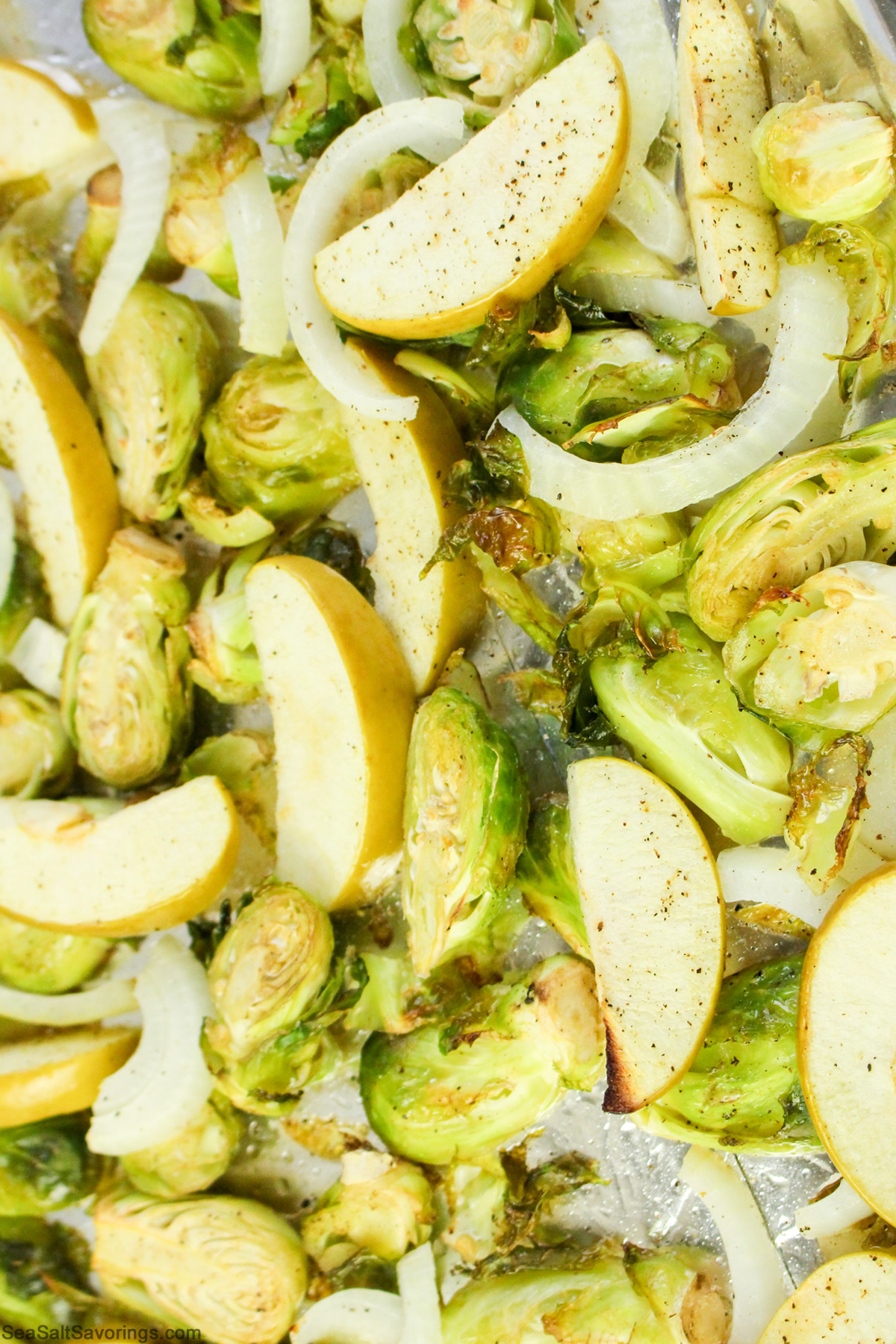 sliced apples and brussel sprouts on a baking sheet all cooked up