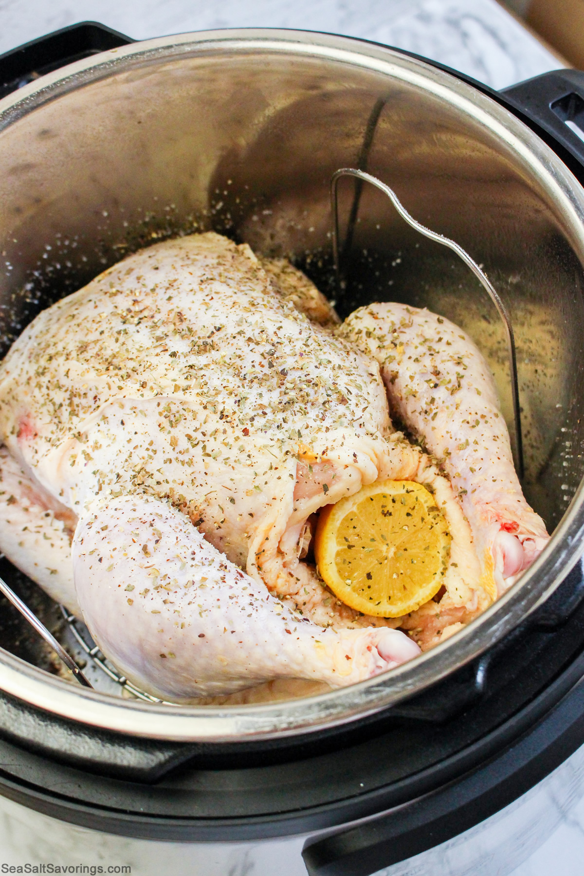 a raw whole chicken placed in instant pot with an orange wedge stuffed in it