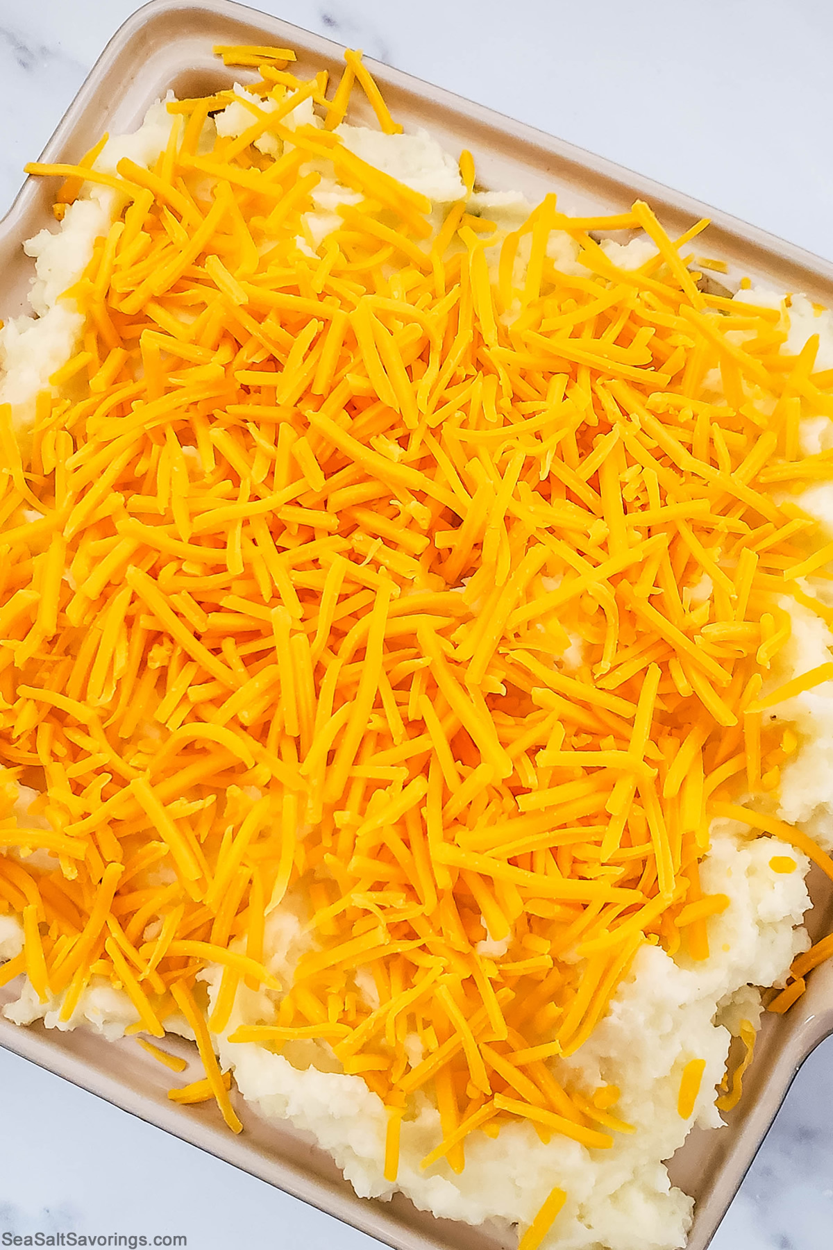 baking dish with cheese added on top of mashed potatoes and pie filling