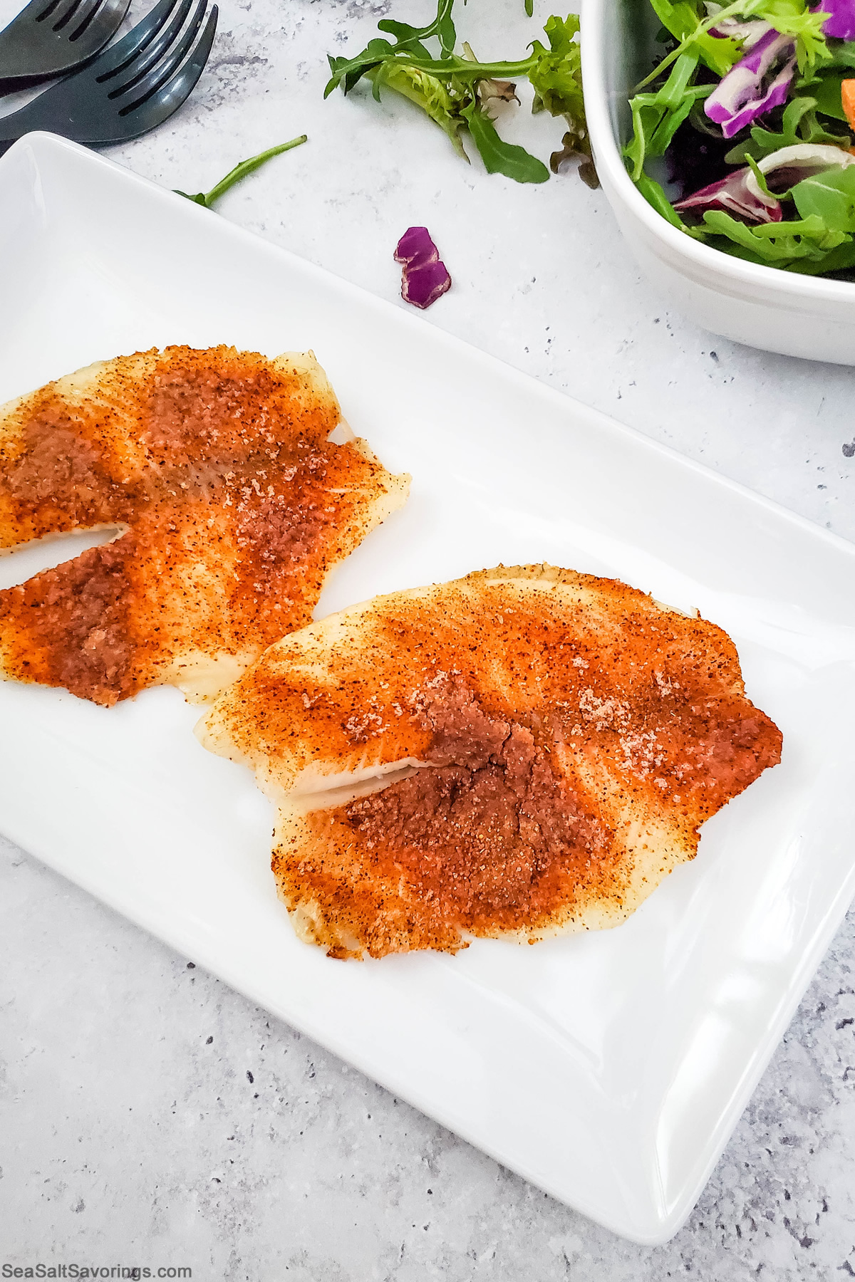 two baked tilapia covered in season on a plate