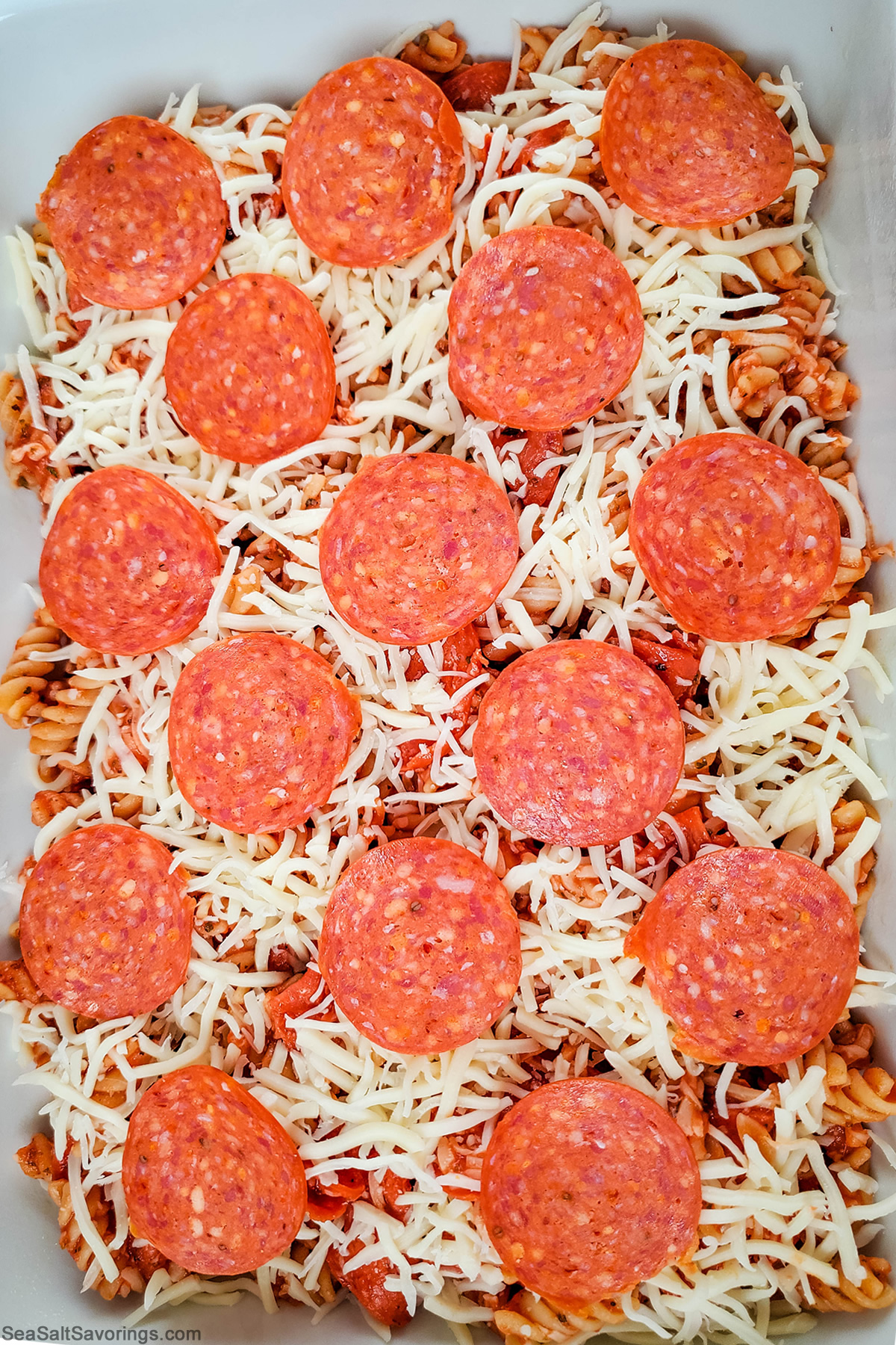 topping the baking dish of casserole with cheese and pepperonis