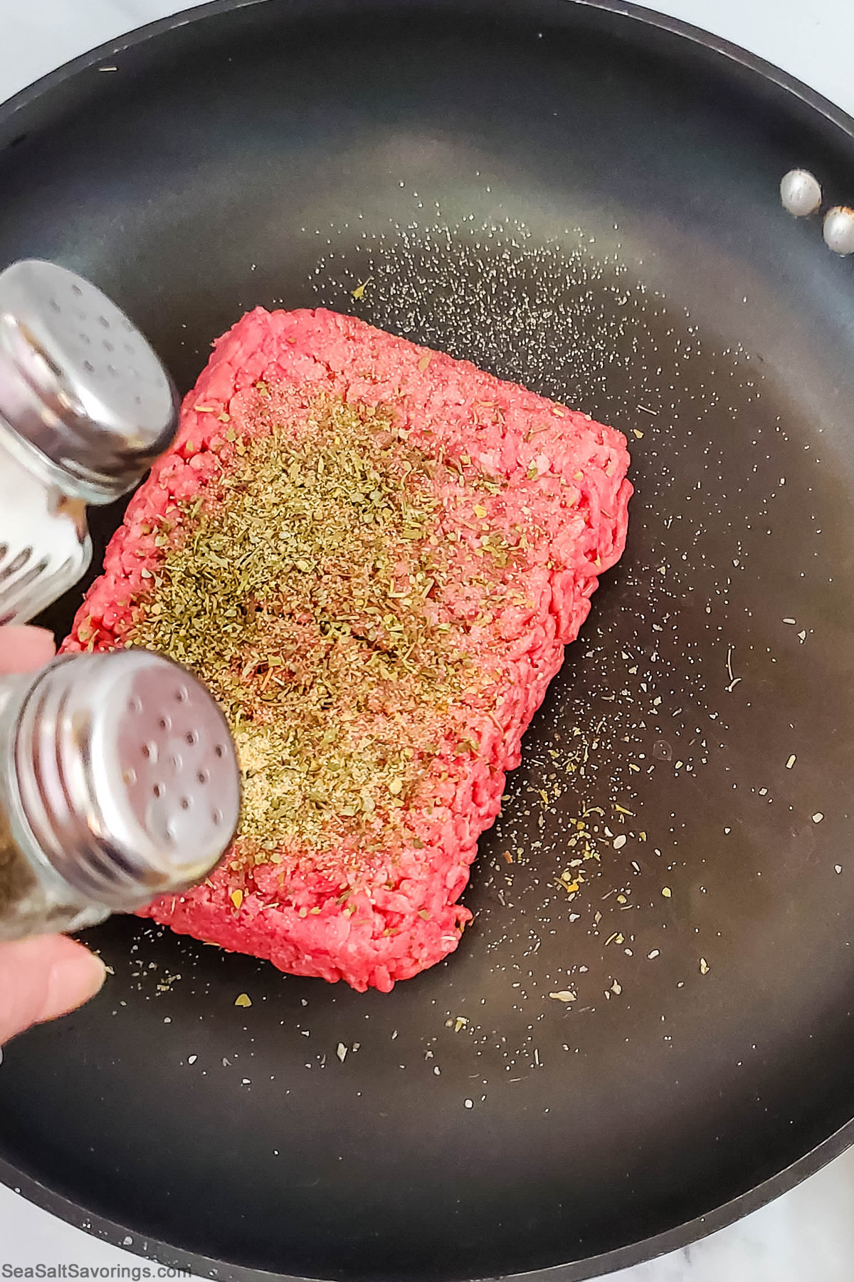 slab of ground beef placed in skillet and seasoned