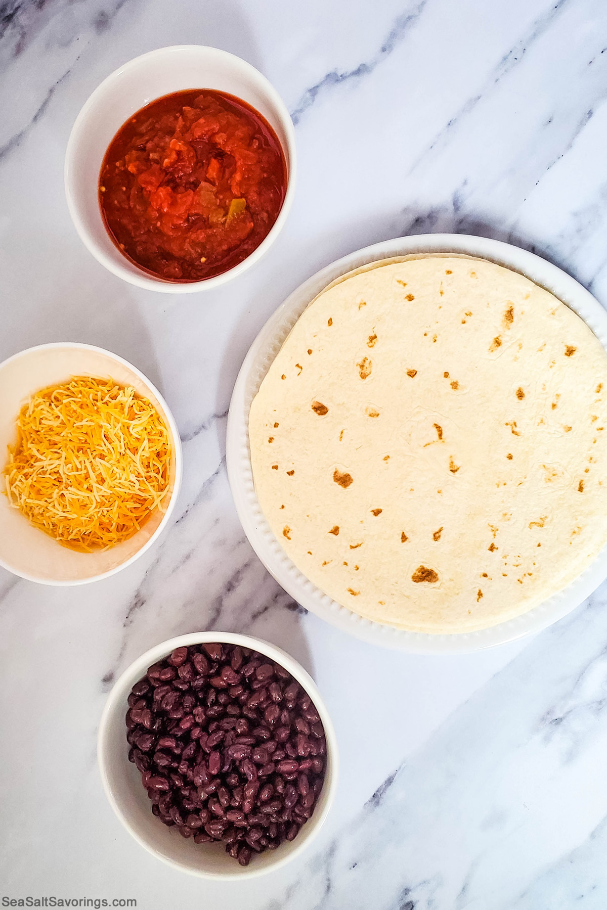 ingredients on a table featuring tortillas and black beans and cheese