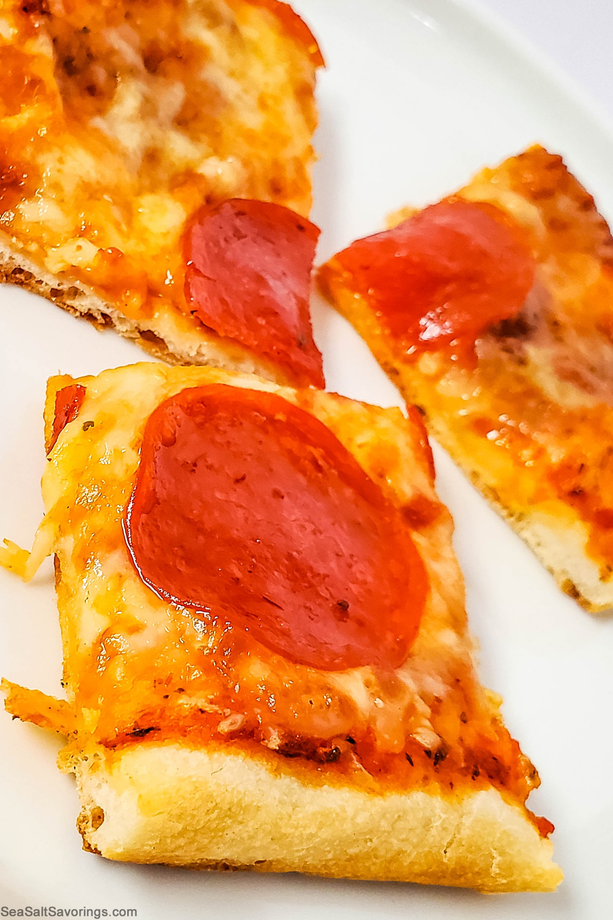 close up view of a square of pizza detailing the melted cheese and crispy crust