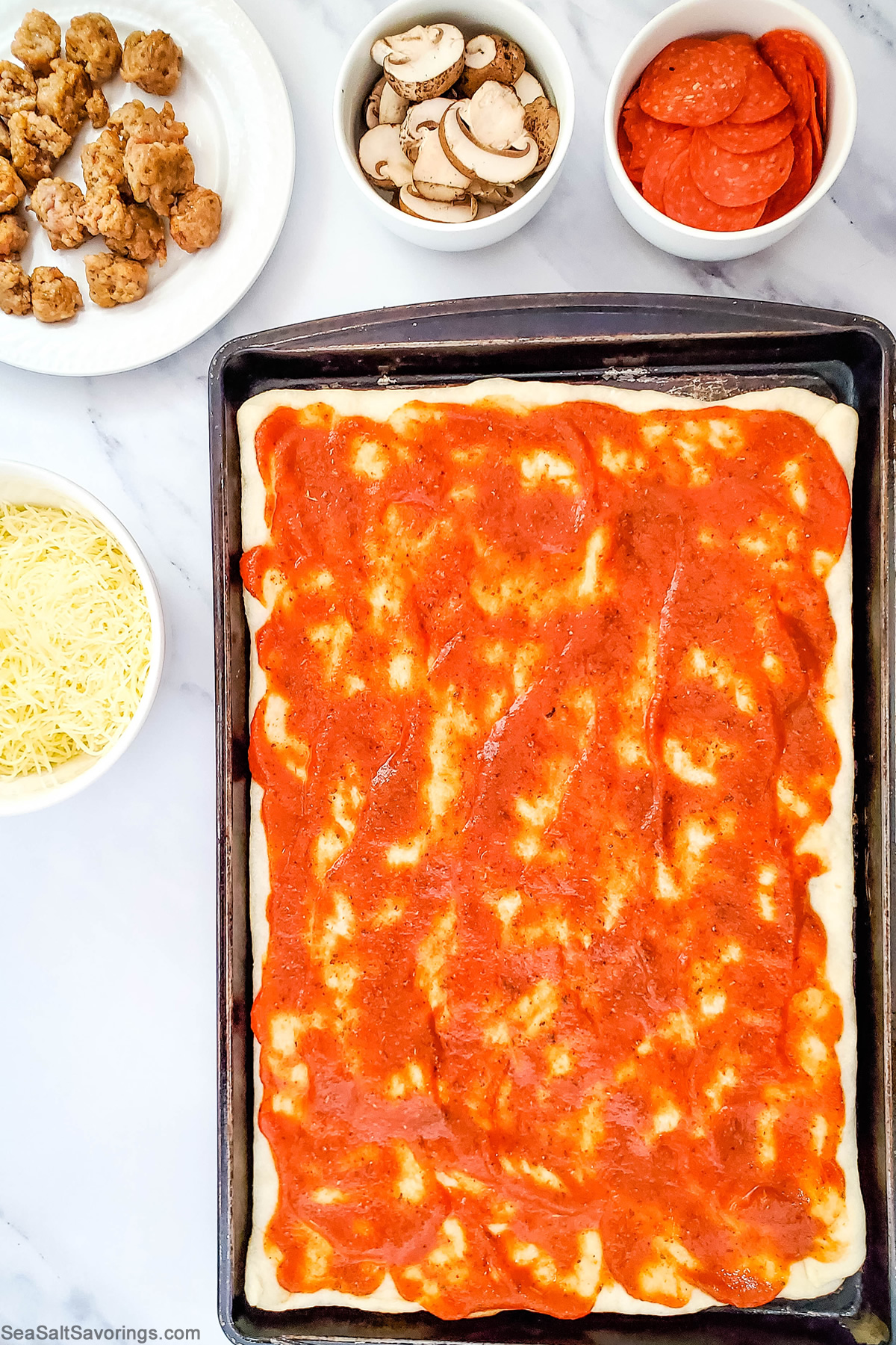 pizza dough spread out on cookie sheet with sauce spread on top