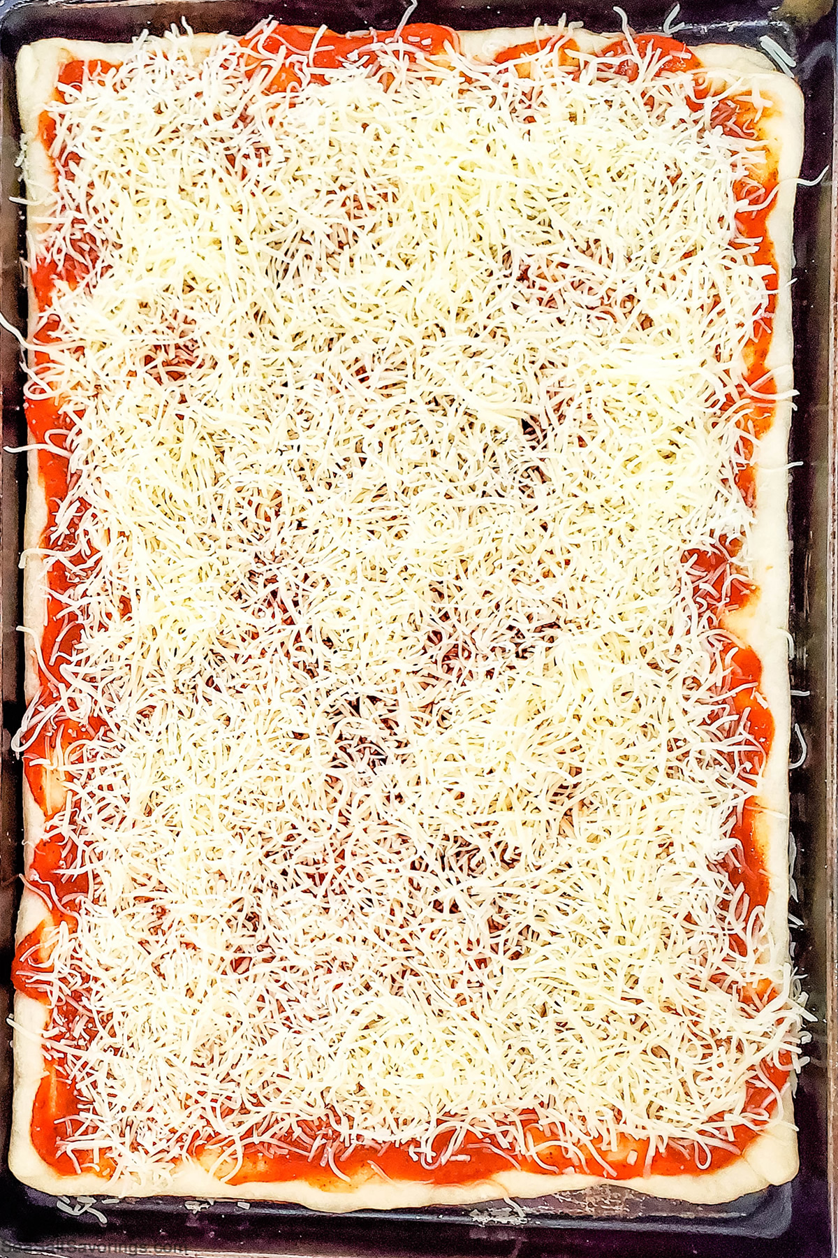 cookie sheet with pizza placed on top with sauce and cheese