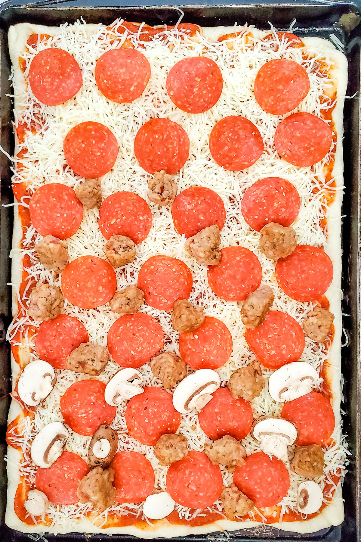 cookie sheet with pizza ready to cook and its topped with cheese and sausage and pepperoni and mushroom