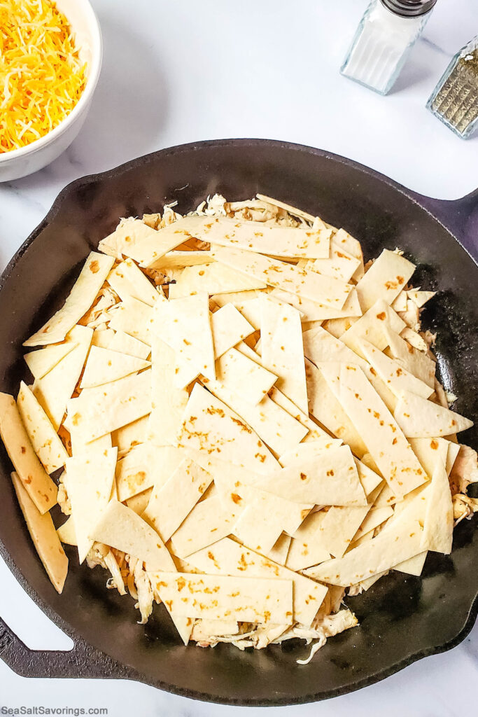 slices of tortilla placed on top of shredded chicken in a skillet