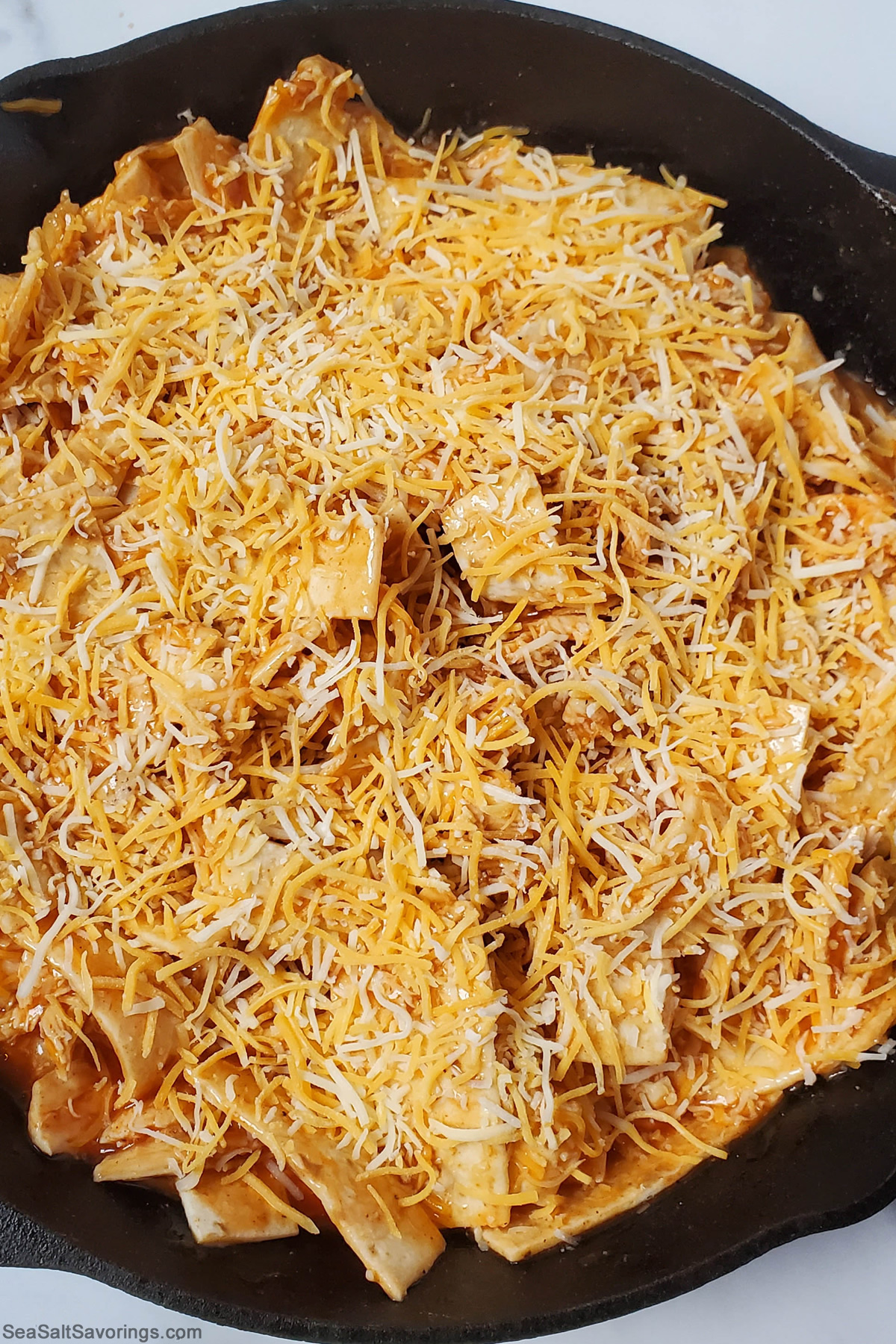 completed skillet enchilada dish ready to go into oven with cheese sprinkled on top