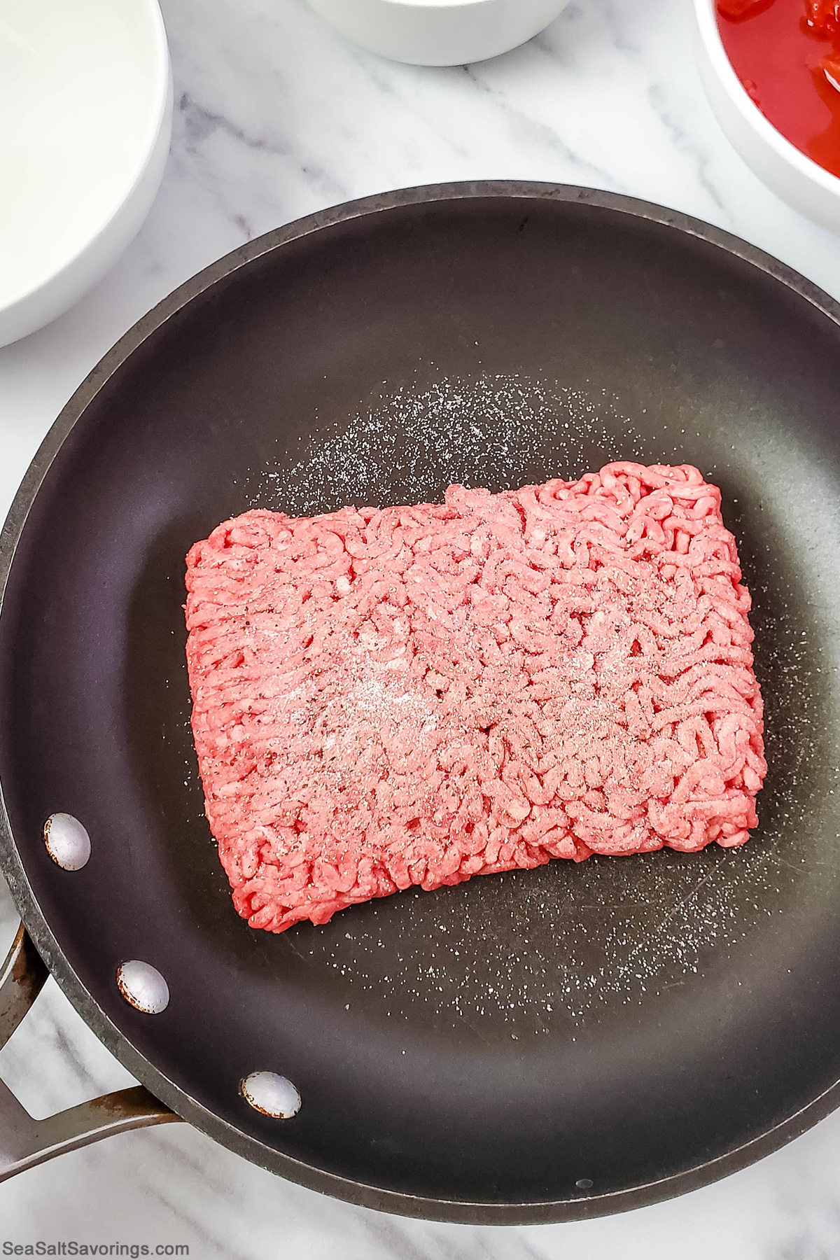 slab of ground beef plopped in a skillet and seasoned