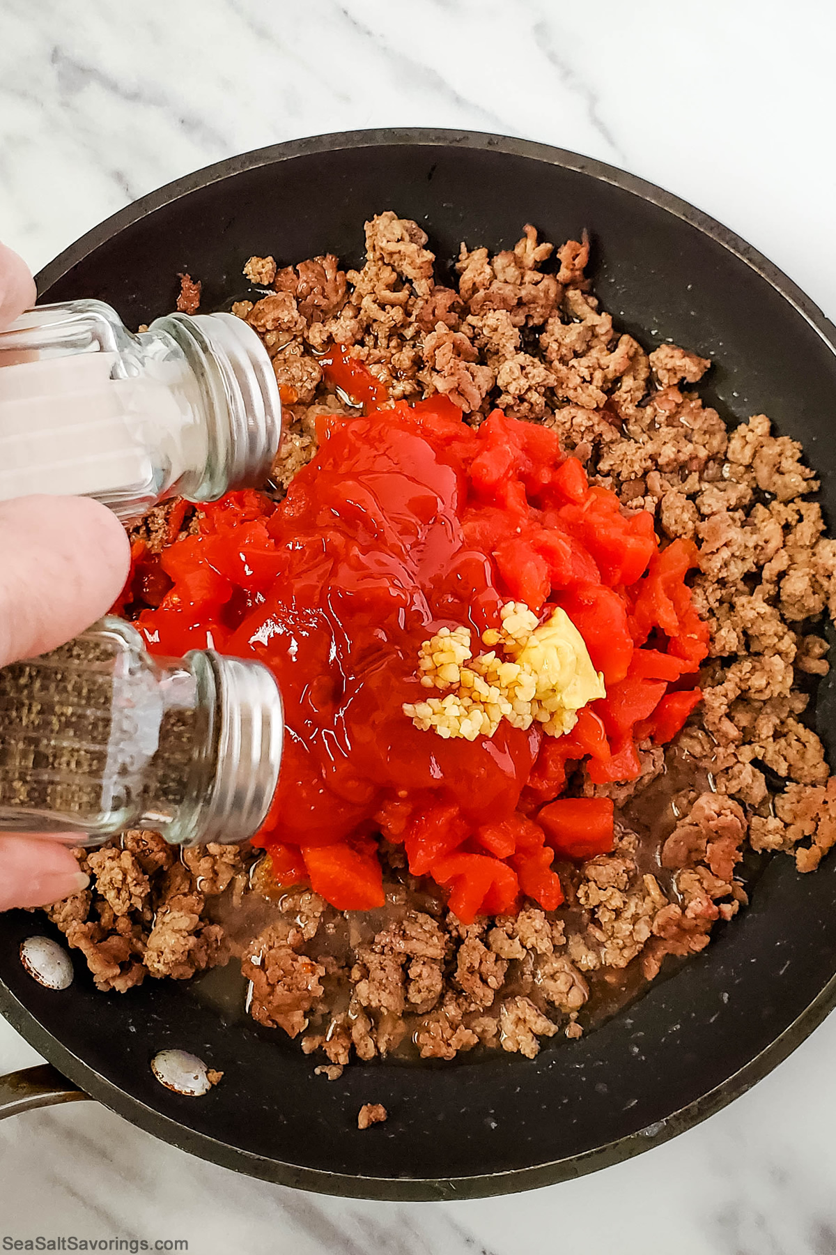 cooked ground beef in a skillet with tomatoes and ketchup and seasoning added on top