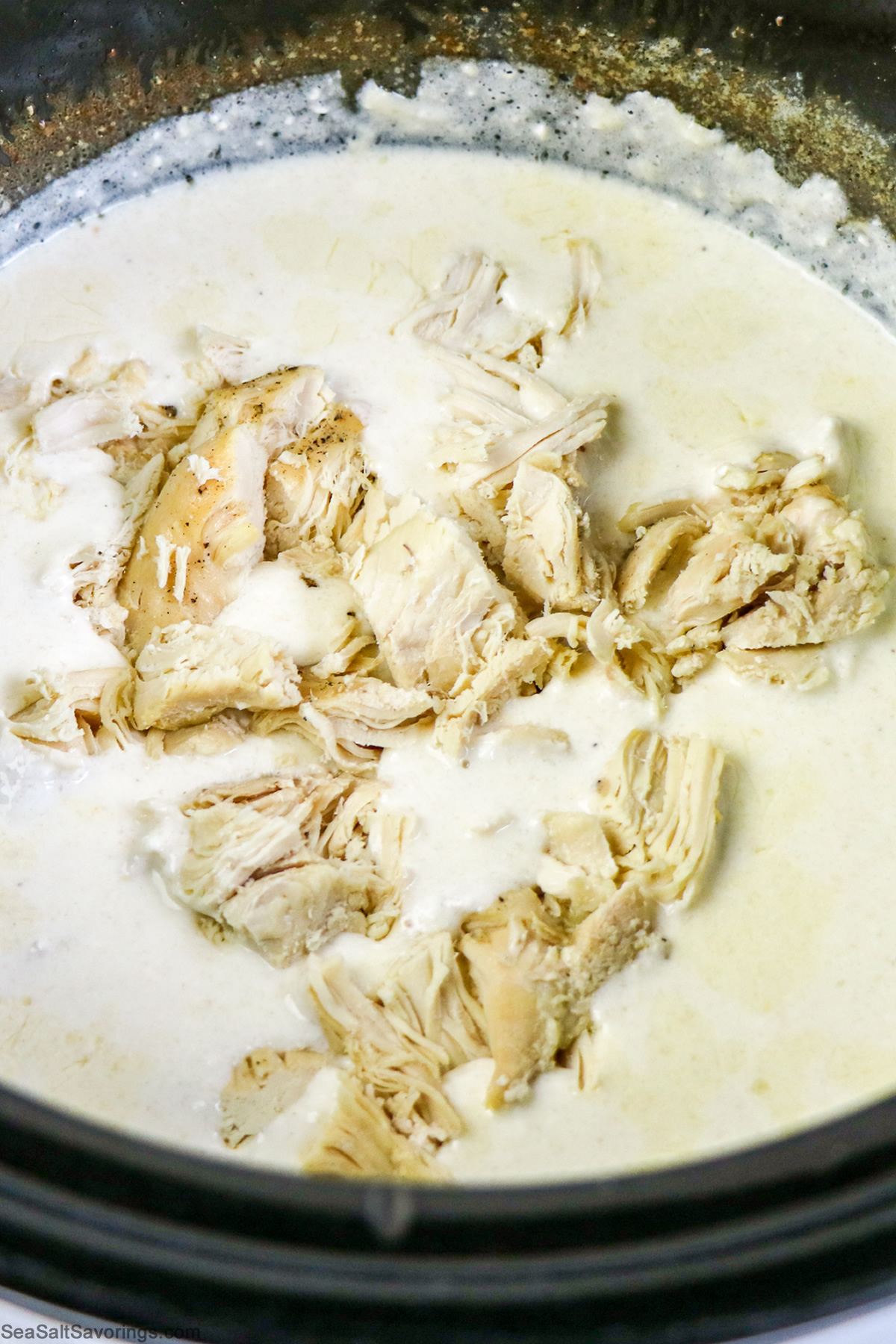 ingredients cooking in the slow cooker, the chicken looks shredded and cooked and covered in a creamy sauce