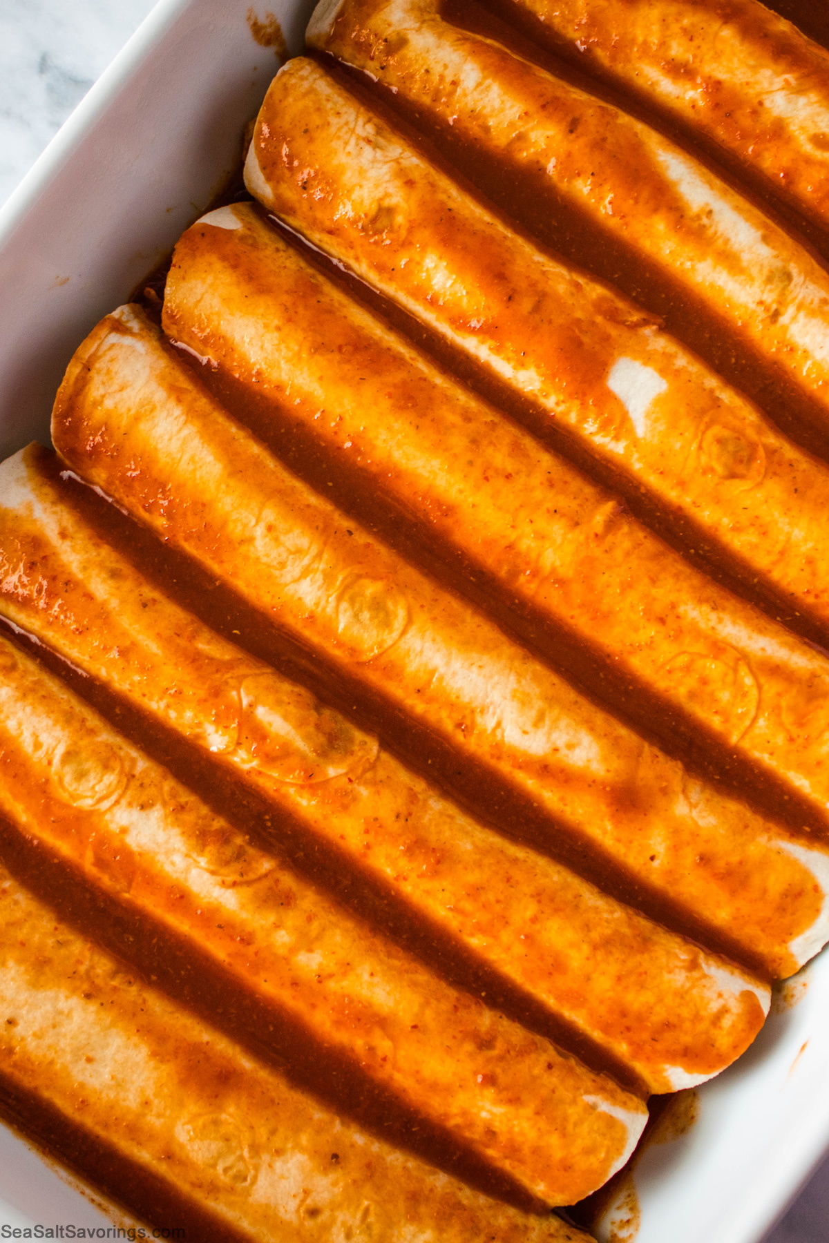 rolled up tortillas placed in baking dish and sauce poured on top of them