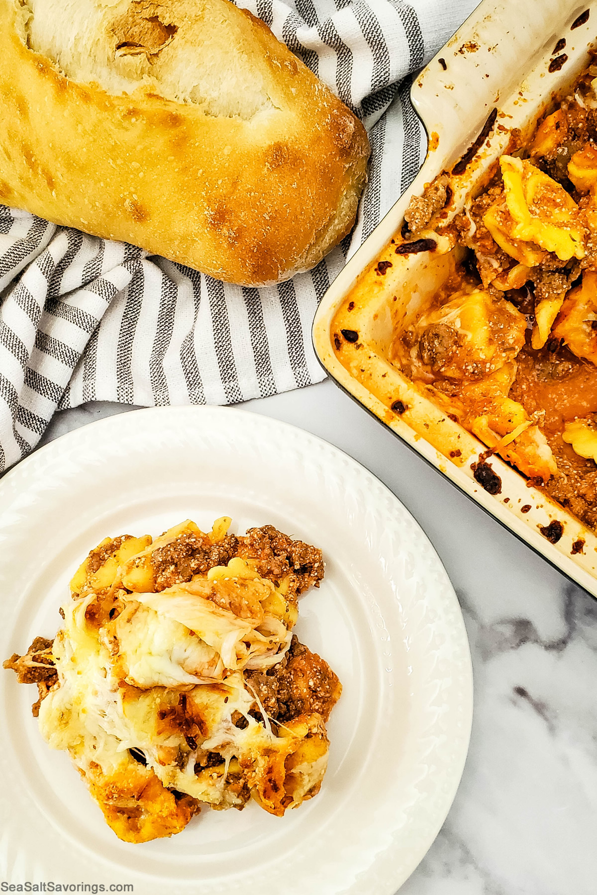 baked tortellini on a plate with a loaf of bread and the casserole baking dish off in the corner