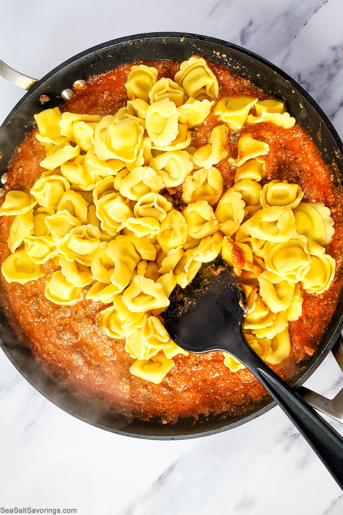 adding tortellini into the sauce in the skillet